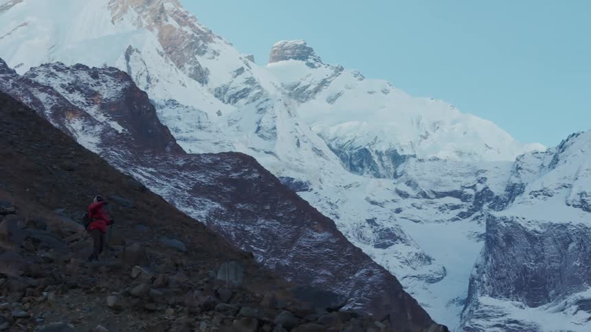 A person in a red coat hikes along the top of a rocky mountain