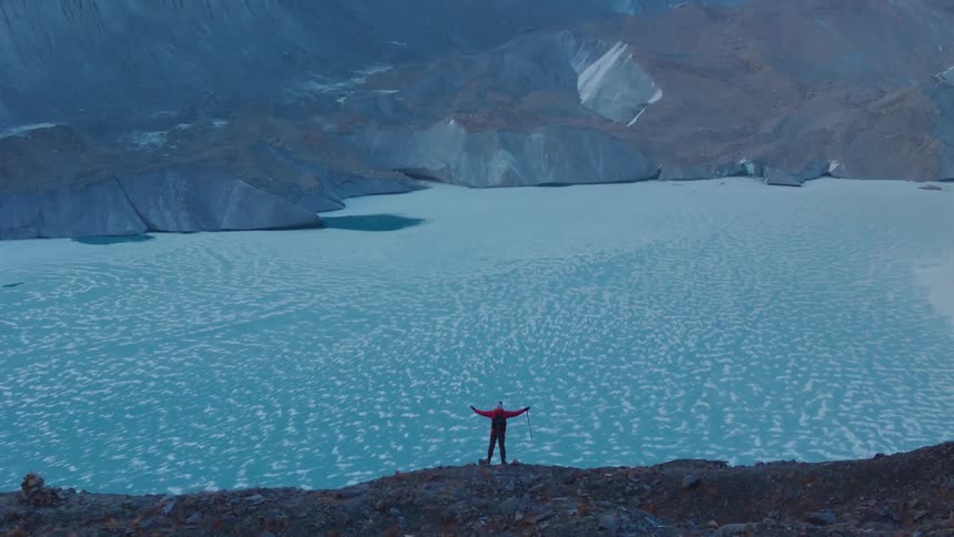 A person standing with open arms looking at a landscape of a lake with mountains in the background