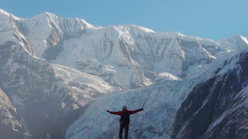 Person with open arms on a cliff with a panoramic view of mountains covered in snow