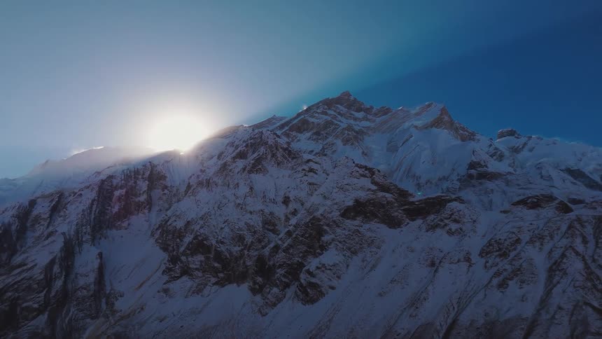 A snow covered mountain peak with the sun either rising or setting behind it