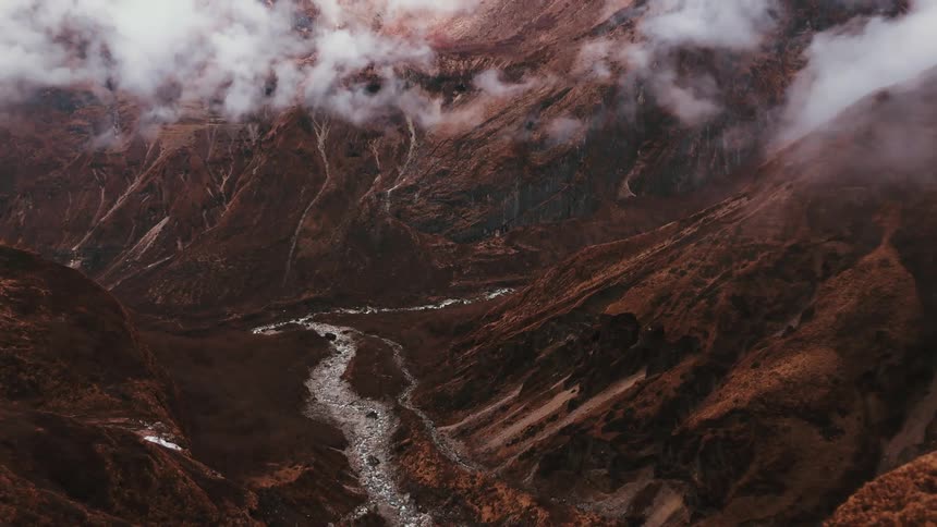 A valley rests among brown mountain peaks enveloped by clouds