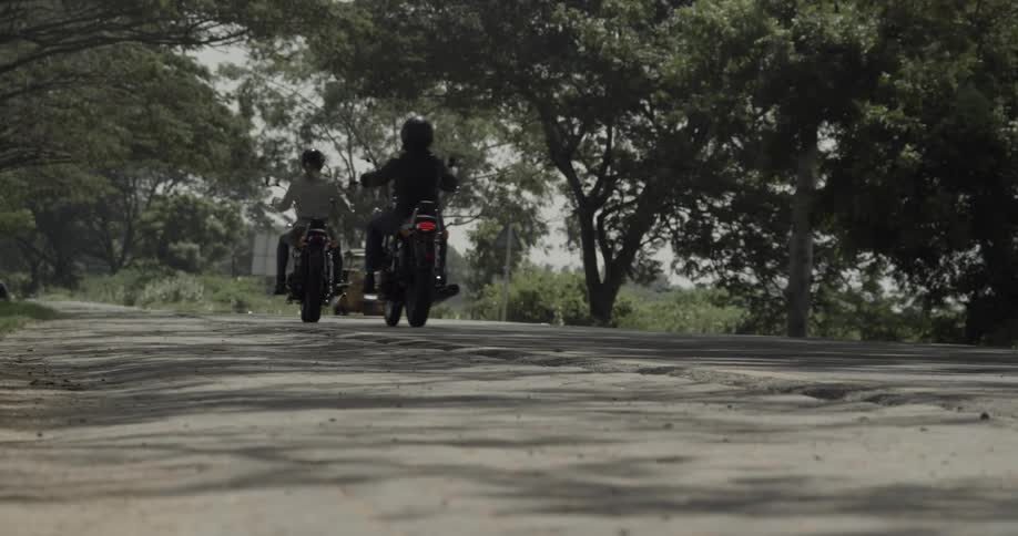 Two people drive motorcycles as a car passes by