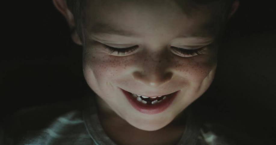 Child laughs while watching a device that illuminates his face