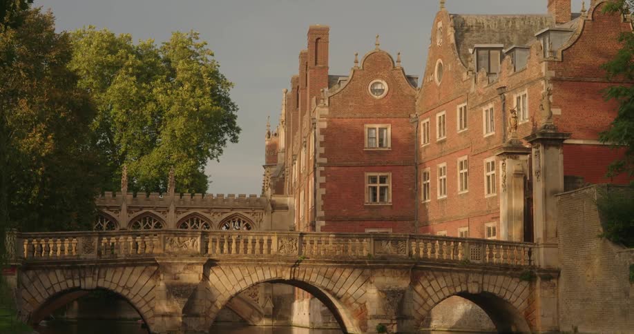 Stone bridge decorated with arches crossing a lazy river with historic red brick buildings in the background