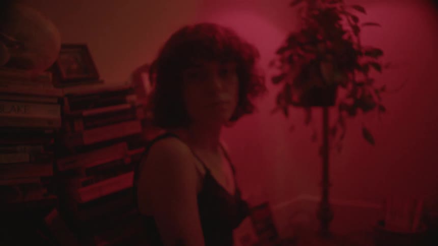 Woman sitting in a red lit room in front of piles of books
