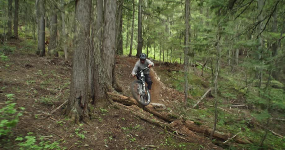 A mountain bike athlete flies underneath the camera after hitting a high-speed jump in the woods