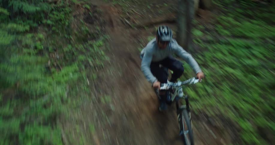 Man mountain biking on a dynamic trail through the forest as seen from cable camera