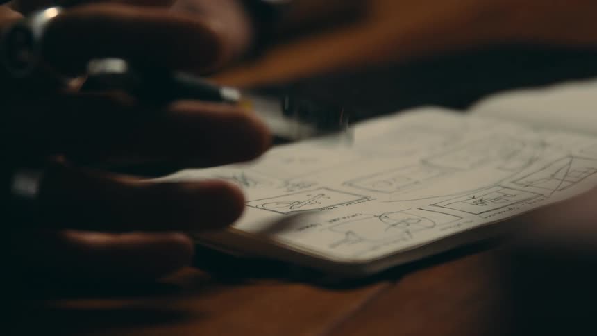 Person taps the end of a pen on an open notebook with drawings already on the page