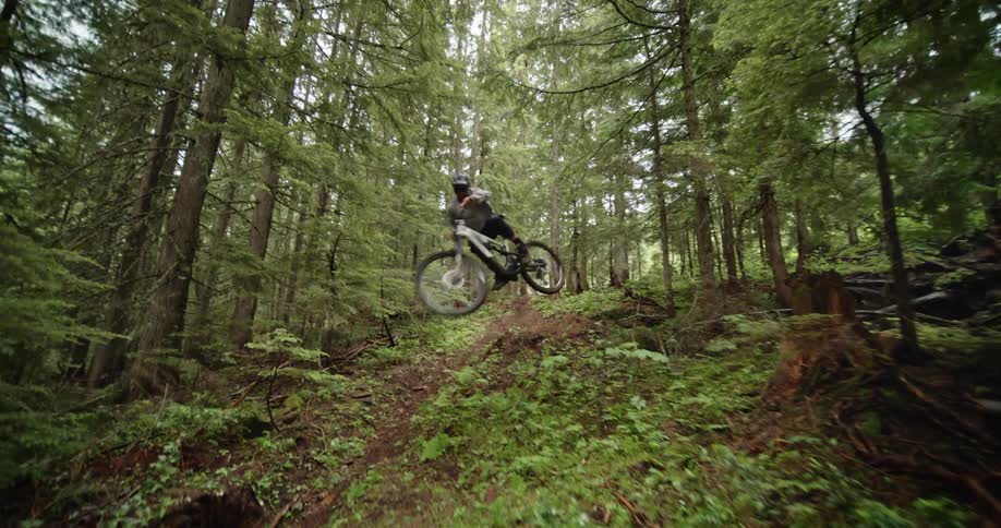 A man riding a mountain bike down a trail in the forest jumps towards camera