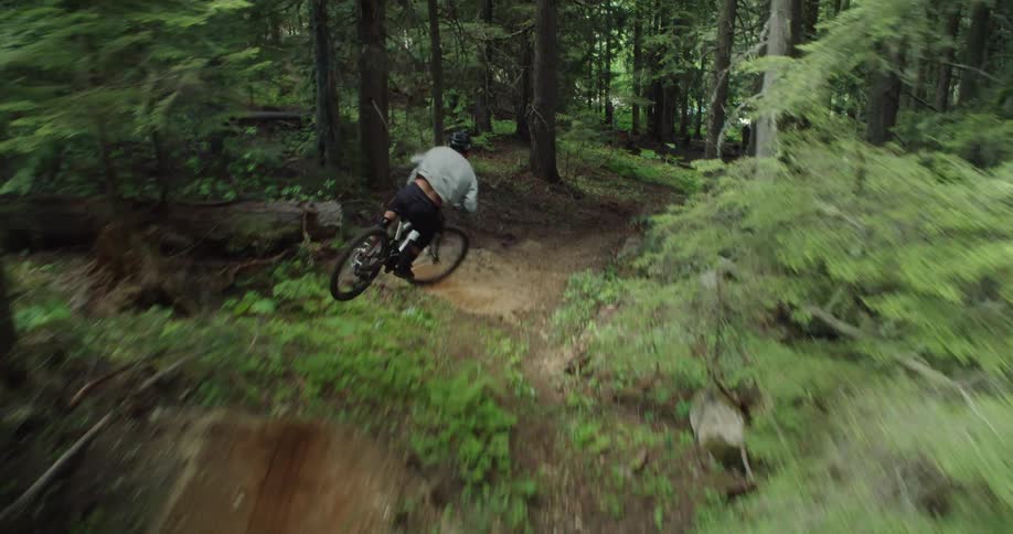 A cable camera perspective chasing a mountain biker down a loose forest trail carving and jumping