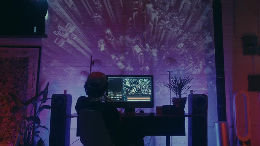 Man sitting at a table with a monitor and an image projected onto the wall in the background in a room with soft blue and purple lighting