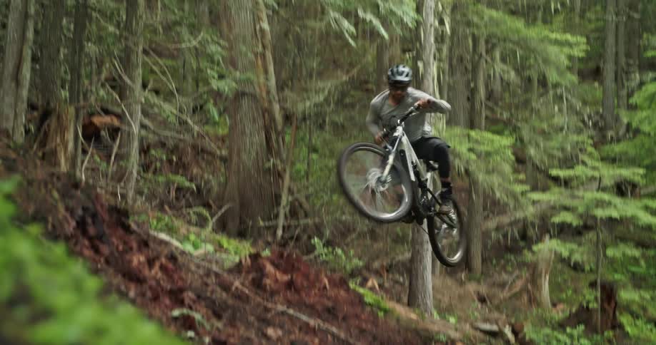 A mountain biker transferring to the high part of a trail off a jump in the forest
