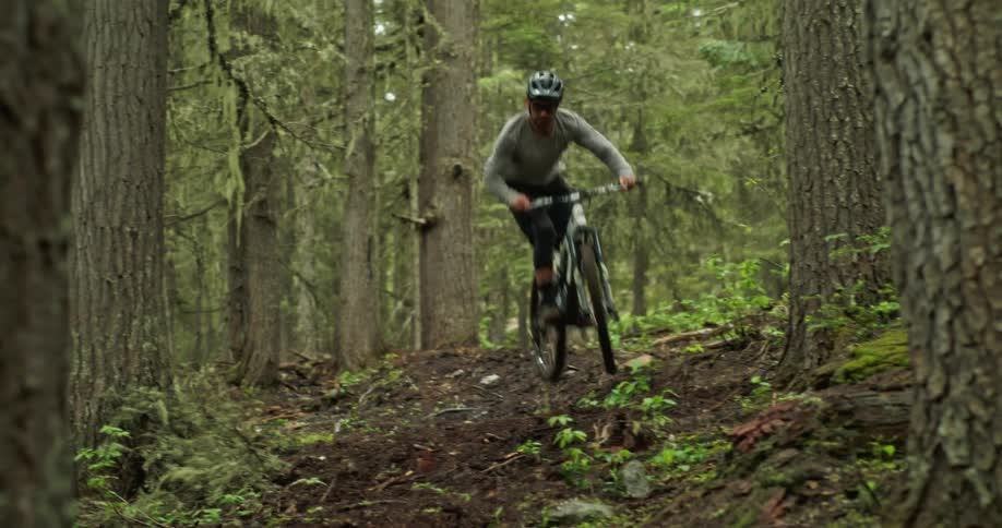 Man jumps and navigates a mountain bike on a loamy forest trail