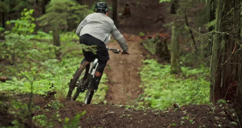 A man riding a mountain bike taps his rear wheel on a piece of the trail while descending