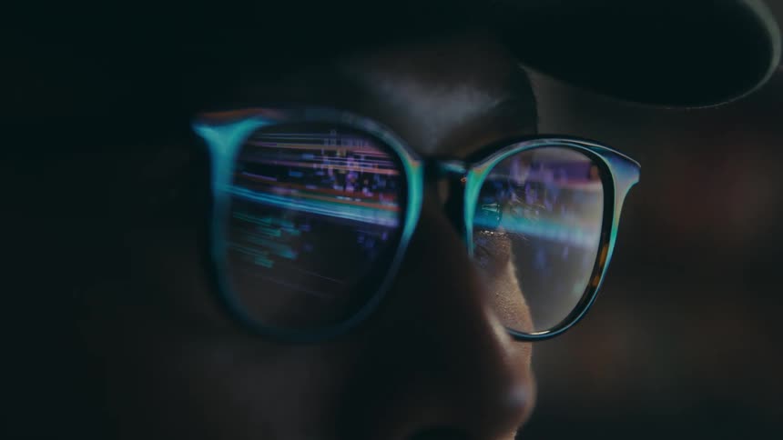 The face of a man with reading glasses that is reflecting lights from a screen