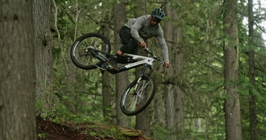 A mountain rider whips his bike sideways off of a jump on his trail