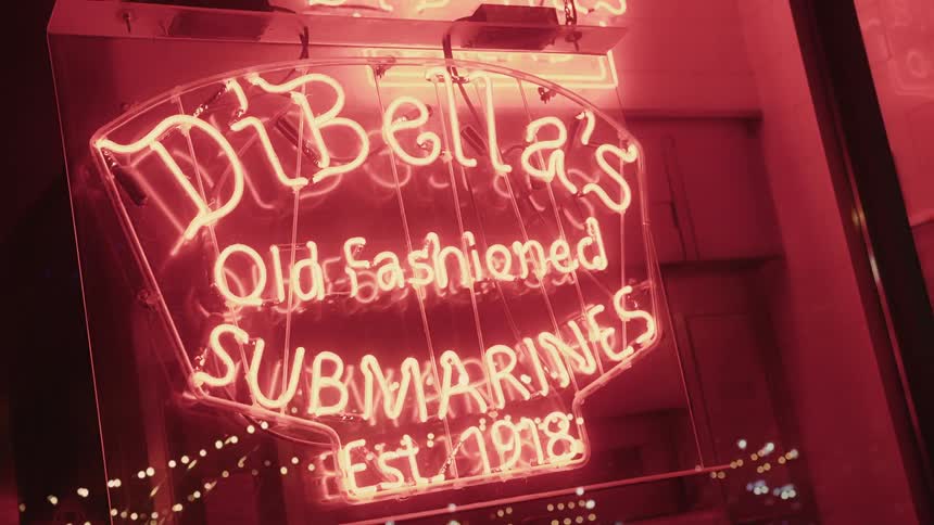 A red neon sign that reads dibellas old fashioned submarines est 1918