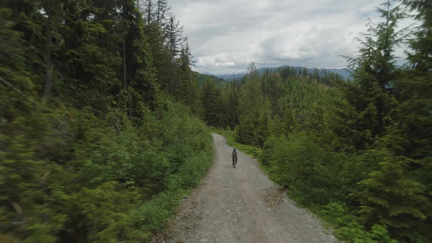 A person rides a bicycle up a gravel road with mountains in the background
