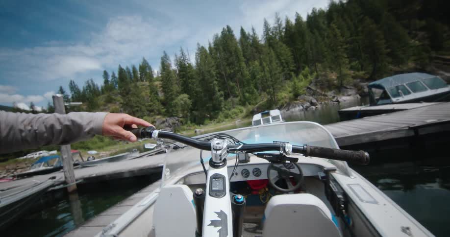A person puts their bicycle onto a boat docked at the edge of a lake