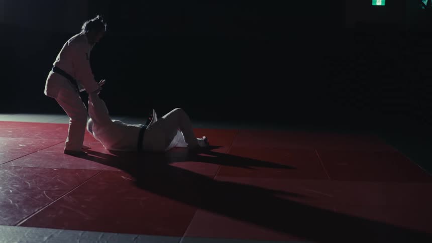 One man flips the other onto the mat while participating in martial arts