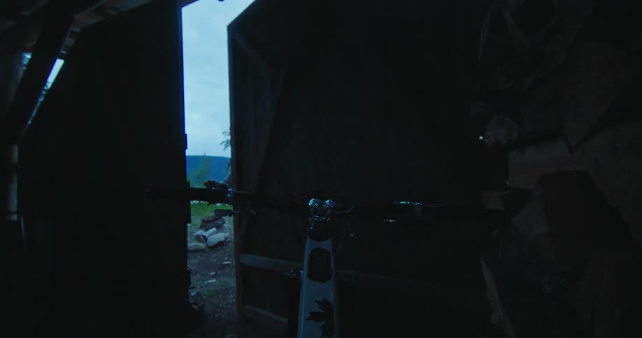 Male cyclist closes the door on a wood shed containing his mountain bike