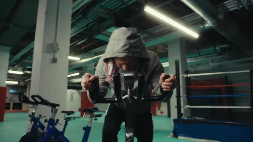 Bearded man pedaling an exercise bike in a gym