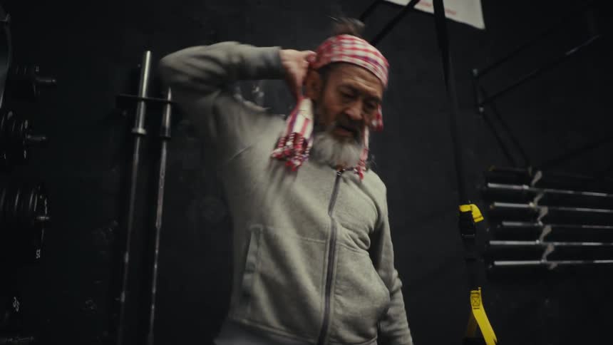 A man with a gray beard has his arm behind his head doing exercises on his right side
