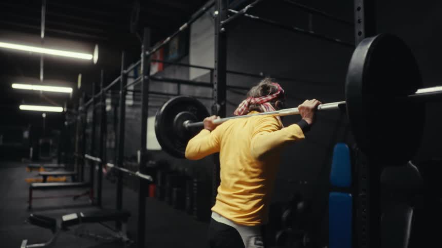 Man puts barbell with two plates on it back onto the rack at the gym