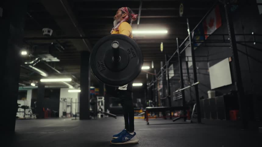 A man in yellow clothing is lifting a weight upwards and then squatting with it