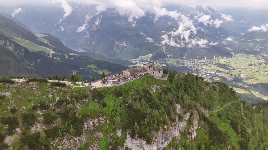 House at the top of a treecovered mountain towering over a neighborhood in the valley