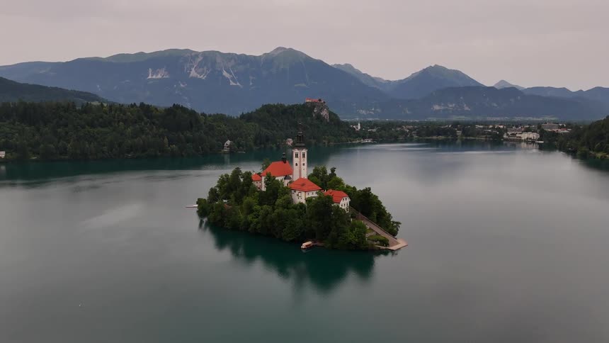 Aerial panorama of a church on an island surrounded by a lake with mountains on the horizon