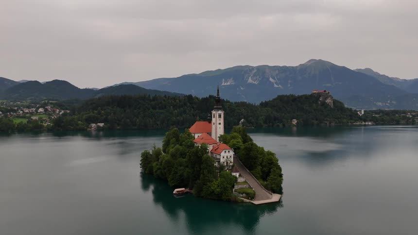 A castle sits on an island in the center of a lake in front of mountains