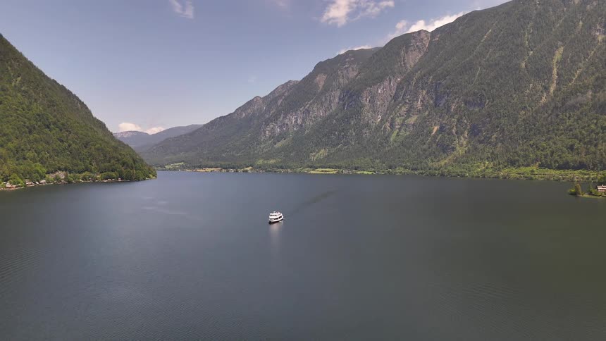 A large boat travels across a lake between two mountain ranges