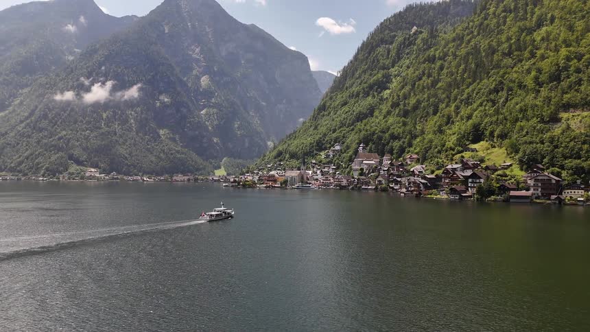 Aerial landscape of a boat on a lake heading towards a village in a mountain valley