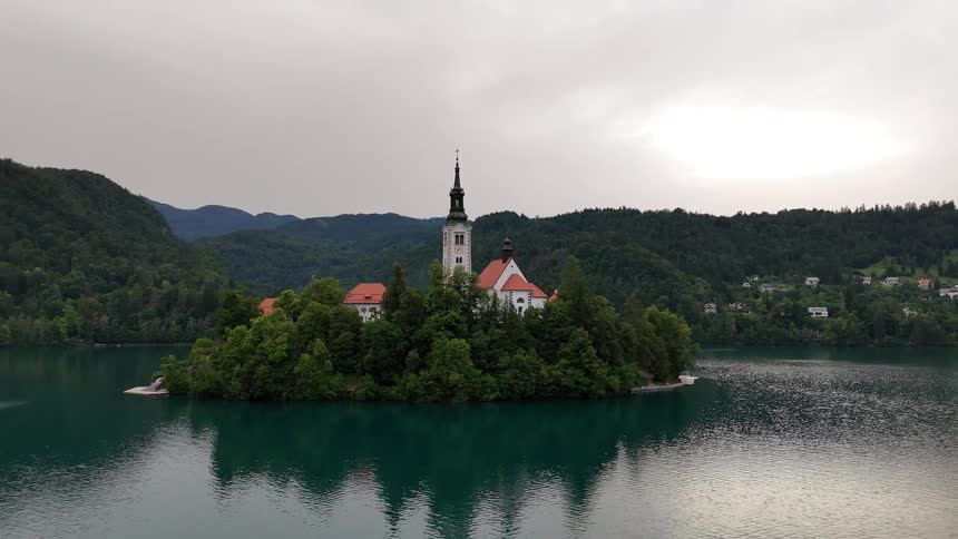 Woods surround the church on an island across the water from a town nestled against a forested mountain