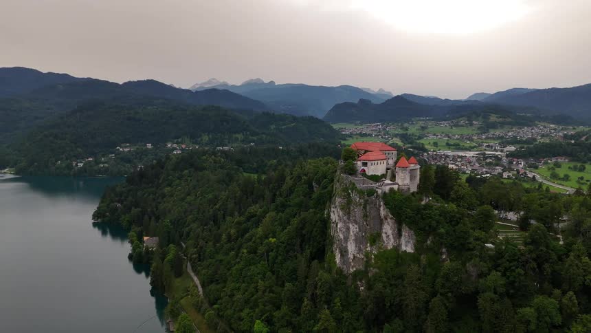Castle situated on top of a cliff surrounded by dense forest and a lake