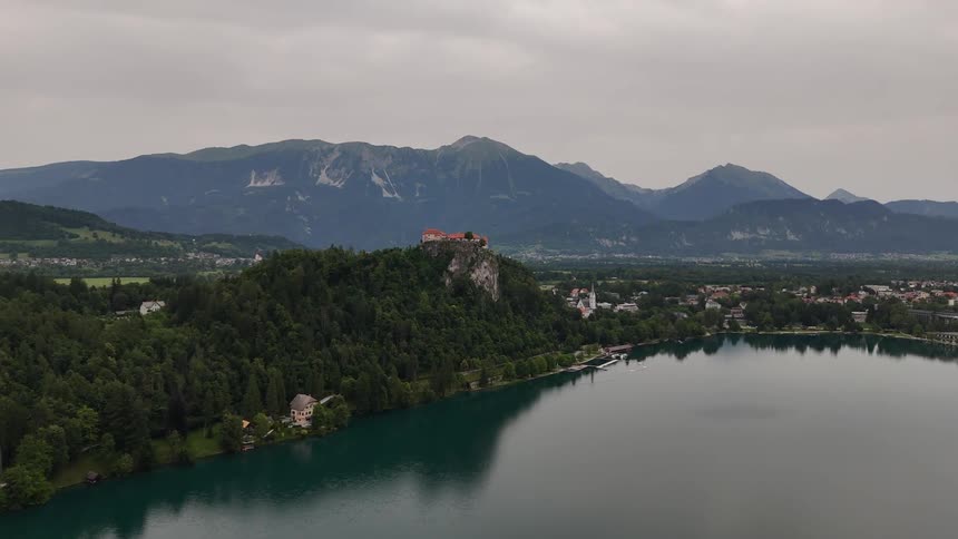 House sitting at the top of a hill overlooking a lake in front of mountains