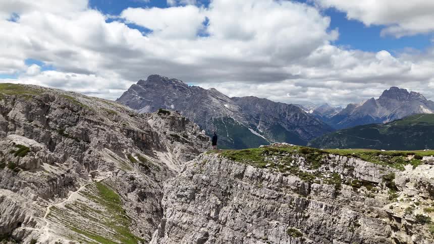 Man standing at the edge of a cliff overlooking mountains across the valley