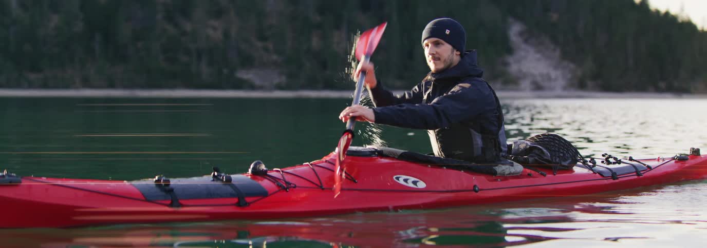 A man is in a red kayak using a paddle to navigate a lake