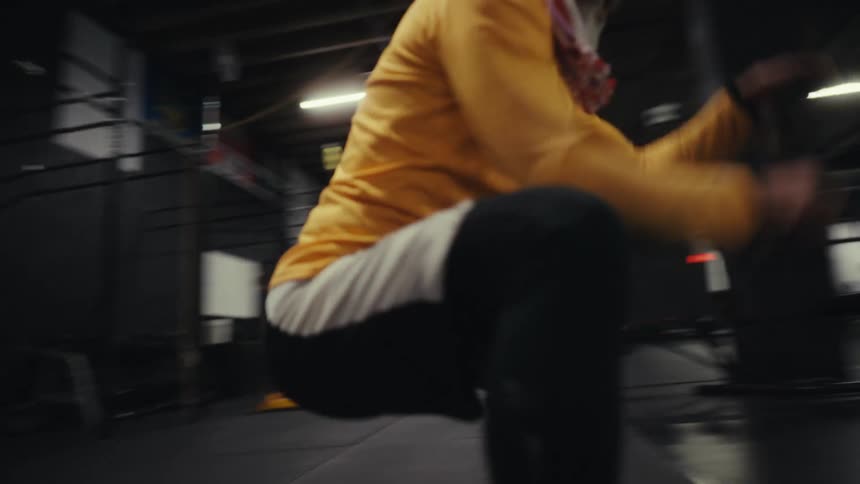 A man in a beanie and yellow shirt is using a rope to train his arm in a gym