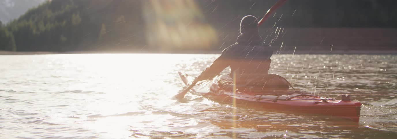 Man paddling a red kayak on a large body of water at sunset