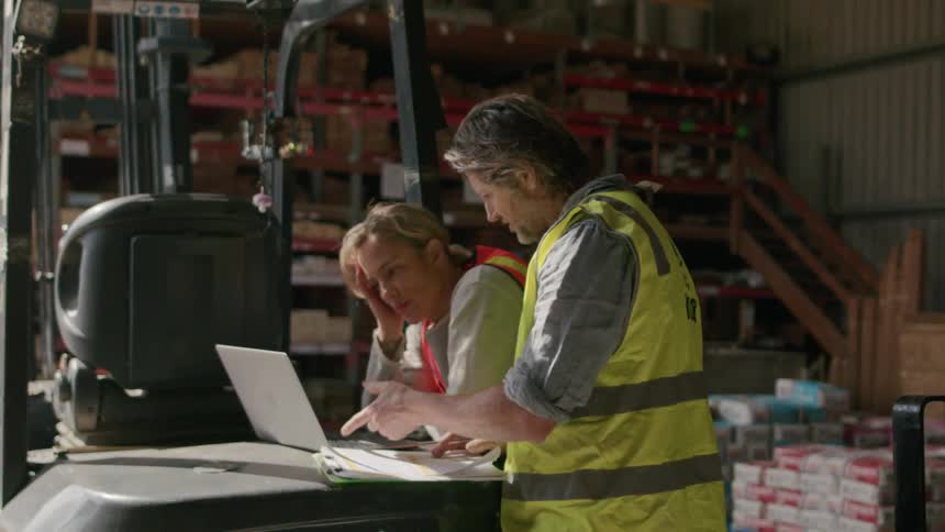 Two workers inside a warehouse talking in front of a laptop
