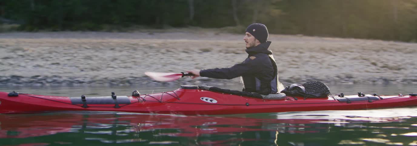 A man is rowing his kayak past the shore
