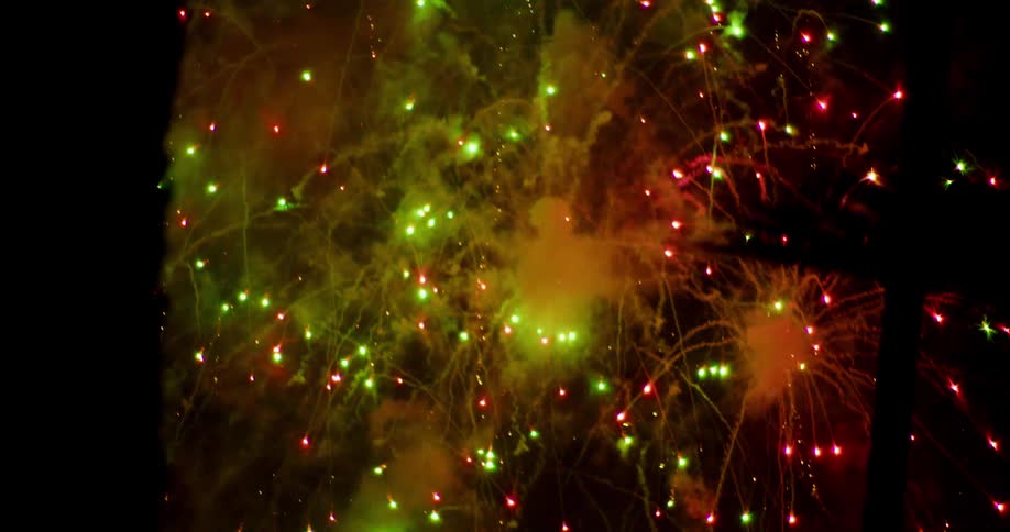 Bright red and green spots trail smoke after fireworks explode in the night sky
