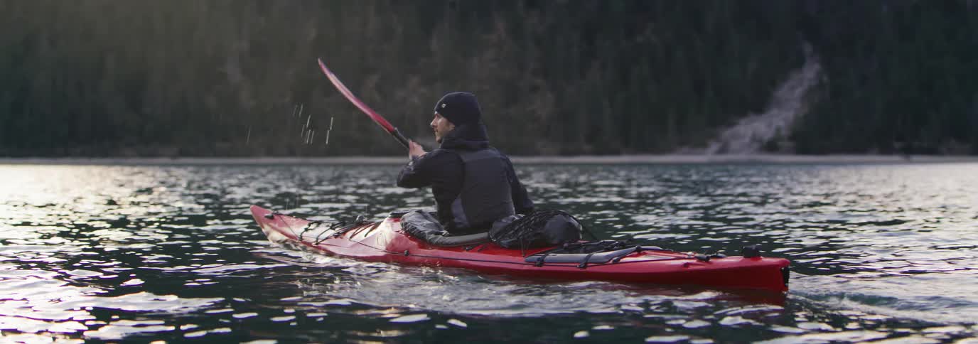 Man paddling a kayak in calm waters with mountains in the background