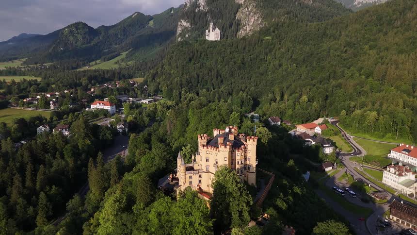 A castle on a hill in a rural town surrounded by trees and mountains
