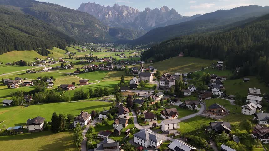 A small rural town in the middle of a large green lawn surrounded by hills of pine forests