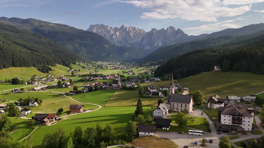 A city with some houses spread across a green field surrounded by hills full of trees
