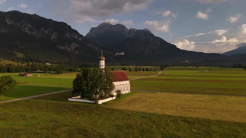 The large white church with the red roof is sitting next to a country road surrounded by fields