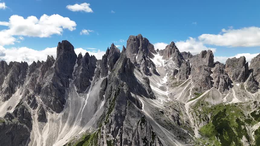 Aerial view of rocky mountains with pointed peaks against a partly cloudy blue sky